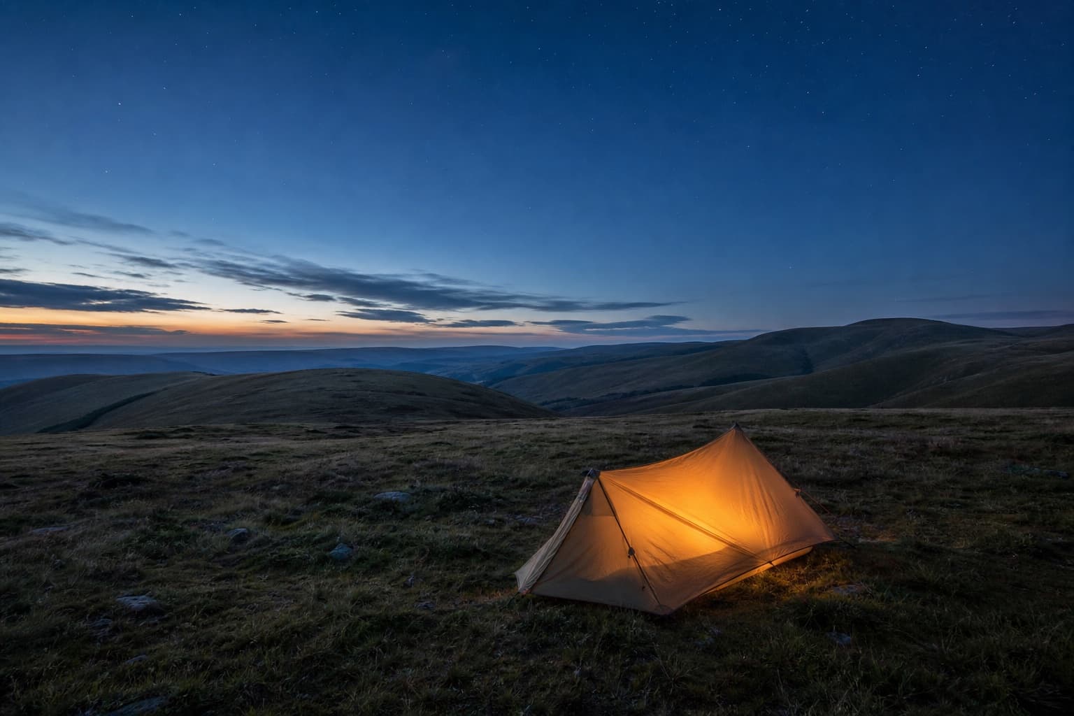 A glowing one-person tent pitched on the open Cheviot fells in Northumberland at dusk under a starry sky