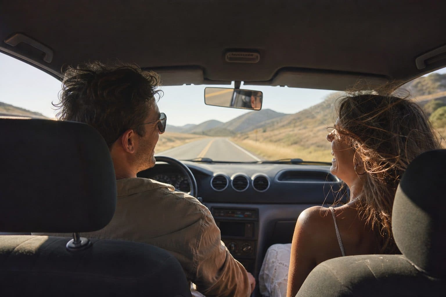 Two adults laughing together in the front seats of a car on an open road